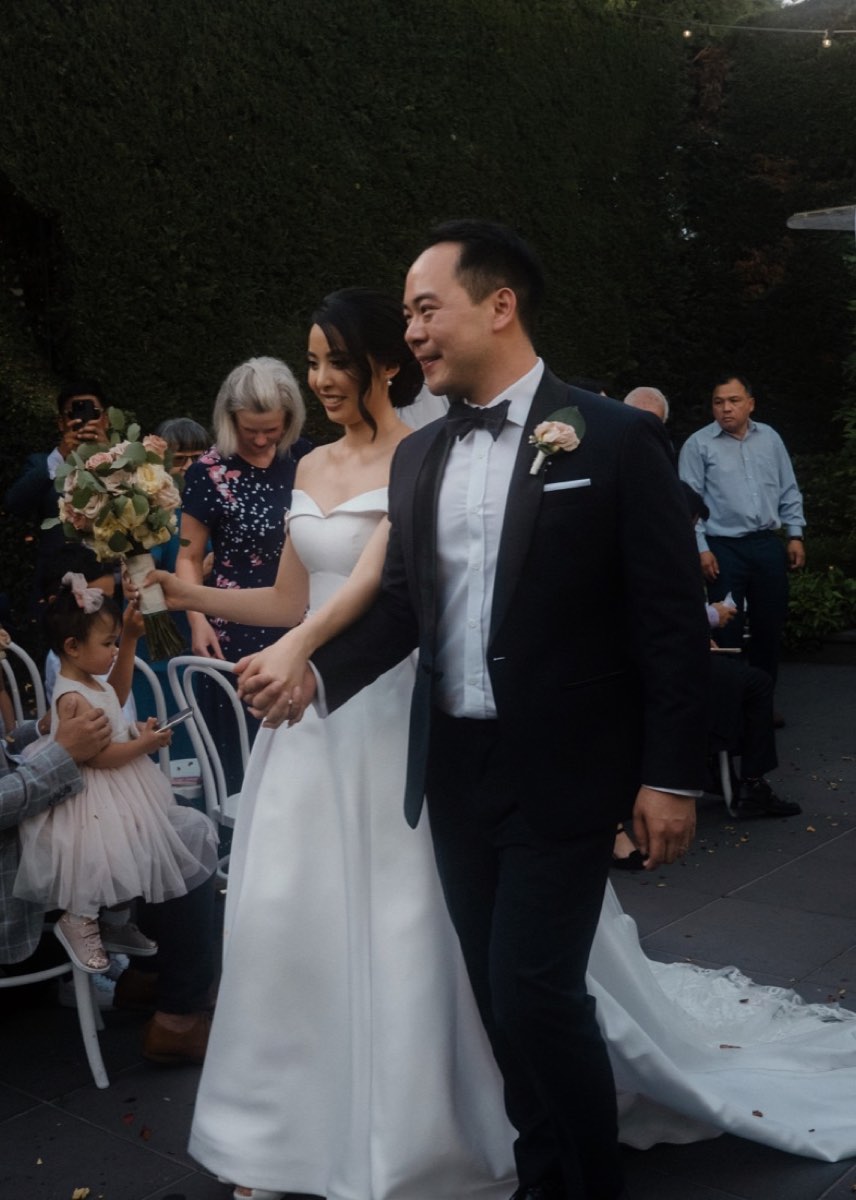 The couple beam as petals fly at the end of a garden ceremony