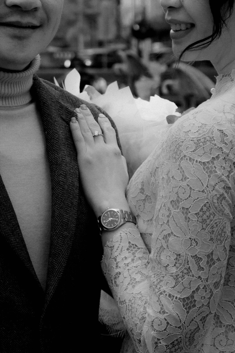 Black and white detail of hands and rings against the lace sleeve of the wedding dress