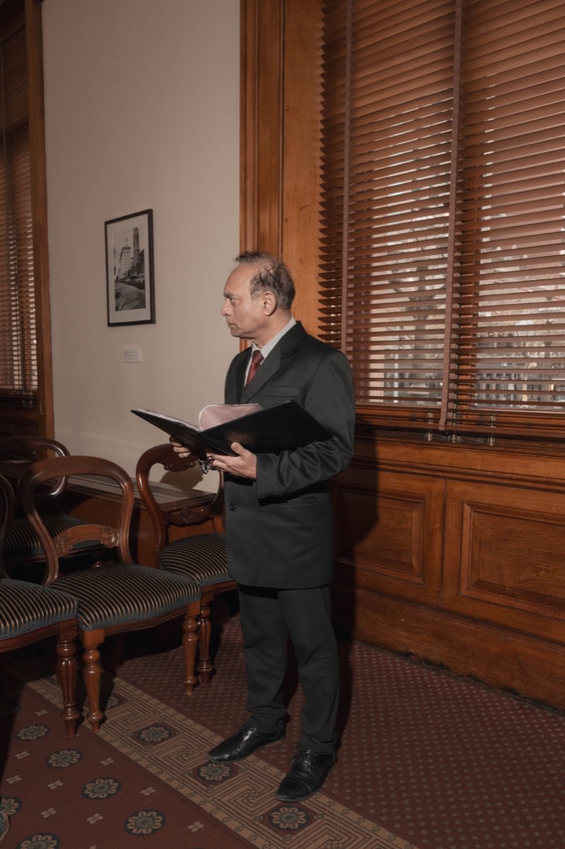 The celebrant reads over his folder by the shuttered window before the ceremony