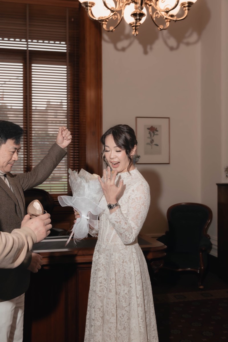 The bride laughs with delight during the ring exchange while a guest cheers behind her
