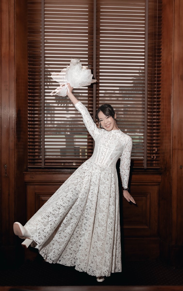 The bride kicks up a heel and swings her bouquet in front of the shuttered window